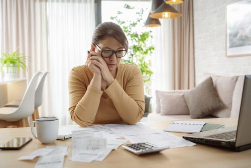 Mature woman contemplating bills and tax papers at home